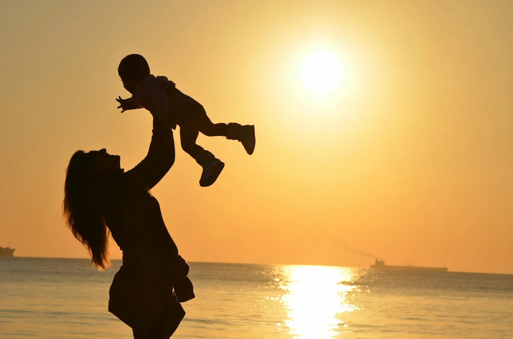 Woman lifting her baby above her head during sunset